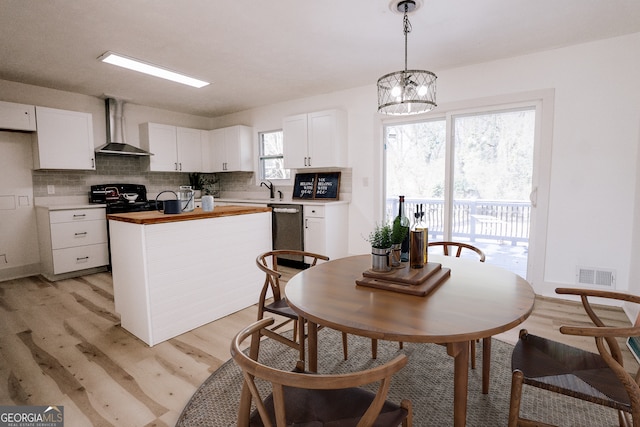 kitchen with white cabinetry, dishwasher, wall chimney exhaust hood, and hanging light fixtures