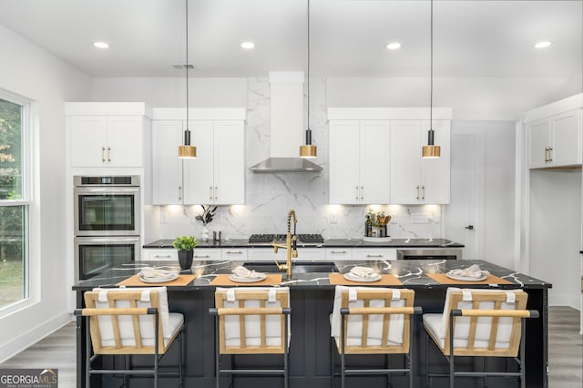 kitchen with stainless steel appliances, white cabinets, and an island with sink