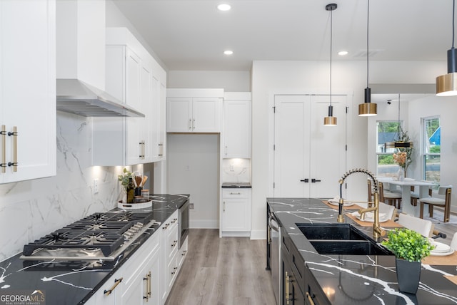 kitchen featuring hanging light fixtures, sink, white cabinetry, wall chimney range hood, and backsplash