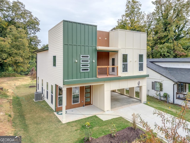 rear view of house with a balcony, central AC, a carport, and a lawn