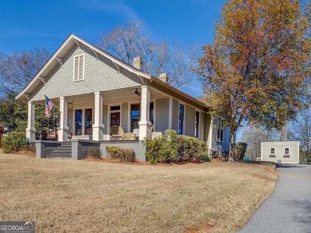 view of front of house featuring covered porch, a front lawn, and an outbuilding