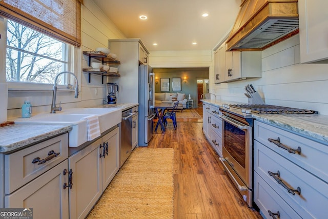 kitchen featuring appliances with stainless steel finishes, gray cabinetry, light wood-type flooring, premium range hood, and sink