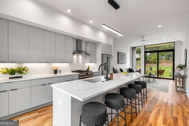 kitchen featuring a center island with sink, high end appliances, wall chimney exhaust hood, and pendant lighting