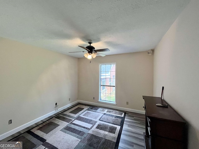 empty room with ceiling fan, dark wood-type flooring, and a textured ceiling