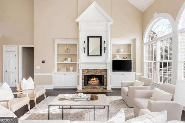 living room featuring built in shelves, a high ceiling, a fireplace, and hardwood / wood-style flooring