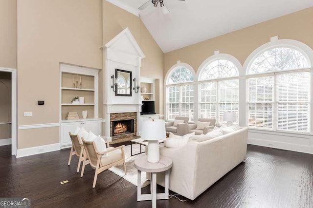 living room with ceiling fan, a healthy amount of sunlight, built in shelves, and a stone fireplace