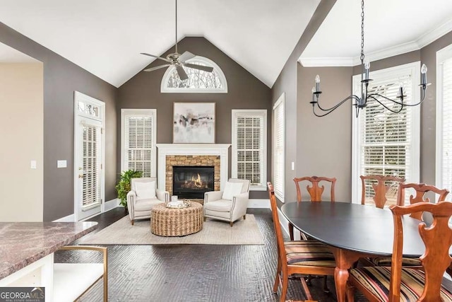 dining space featuring hardwood / wood-style floors, lofted ceiling, crown molding, ceiling fan with notable chandelier, and a fireplace