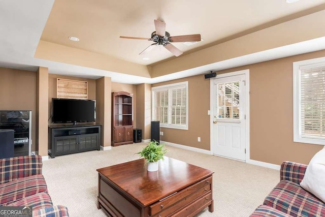 living room with light colored carpet, a raised ceiling, and ceiling fan