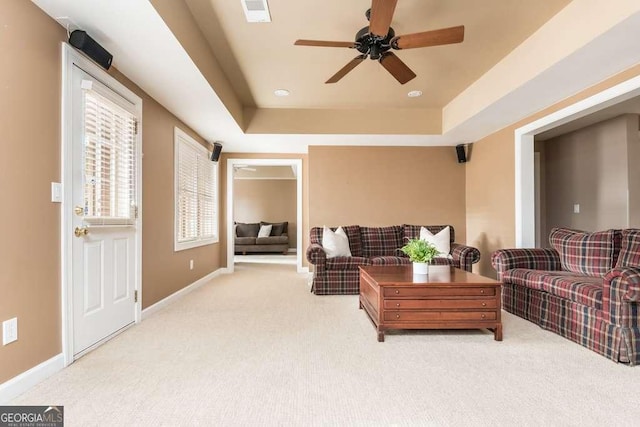 carpeted living room with ceiling fan and a raised ceiling