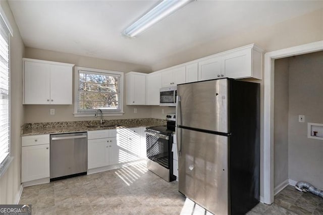 kitchen featuring white cabinets, dark stone countertops, a healthy amount of sunlight, and appliances with stainless steel finishes