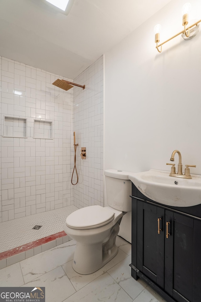 bathroom with tiled shower, vanity, and toilet