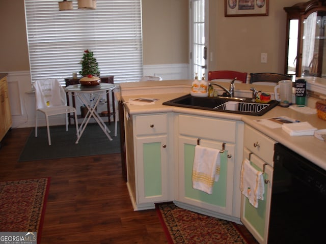 kitchen with black dishwasher, dark wood-style flooring, light countertops, wainscoting, and a sink