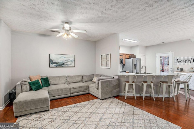 living room with ceiling fan, sink, a textured ceiling, and light hardwood / wood-style flooring