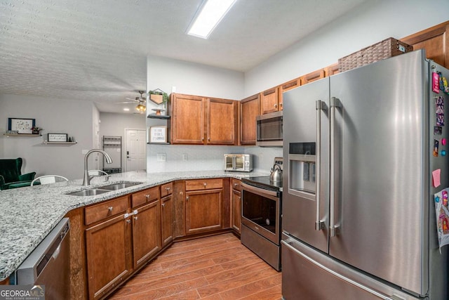 kitchen with stainless steel appliances, light stone countertops, sink, and kitchen peninsula