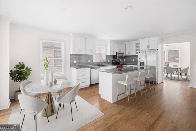 kitchen with appliances with stainless steel finishes, light hardwood / wood-style floors, a center island, dark stone counters, and white cabinets