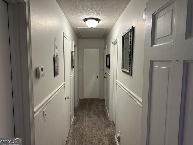 corridor with a textured ceiling and dark colored carpet