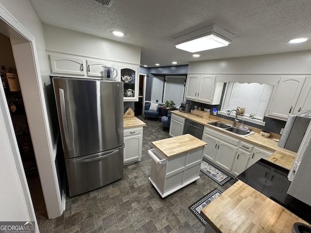 kitchen featuring wooden counters, a textured ceiling, stainless steel fridge, white cabinets, and sink