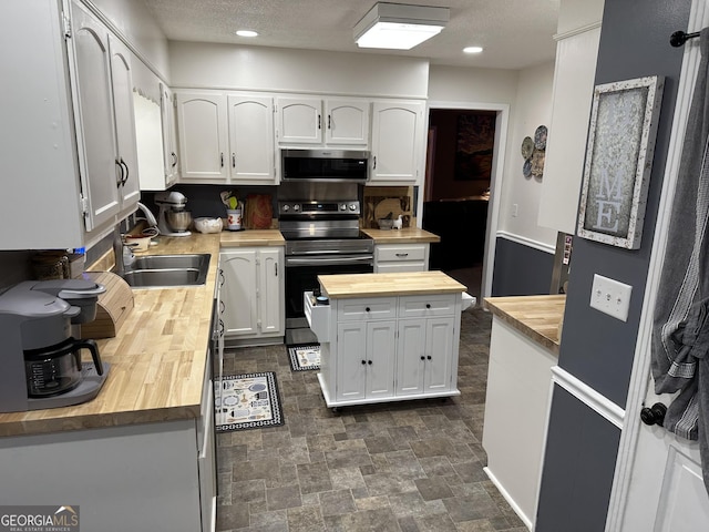 kitchen with a textured ceiling, butcher block countertops, white cabinetry, appliances with stainless steel finishes, and sink