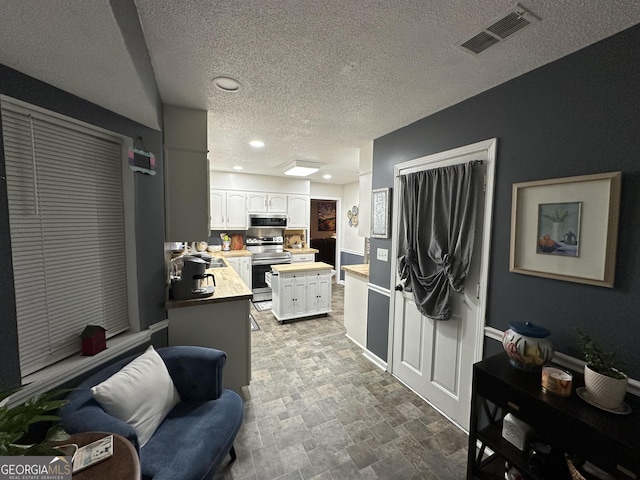 kitchen with stainless steel appliances, butcher block countertops, white cabinetry, and a textured ceiling