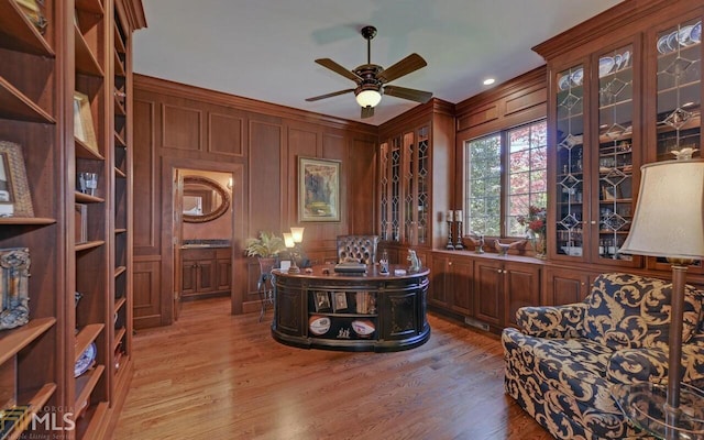 home office with light hardwood / wood-style flooring, ceiling fan, and wood walls