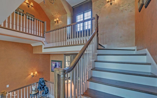 stairs with a notable chandelier, high vaulted ceiling, and hardwood / wood-style floors