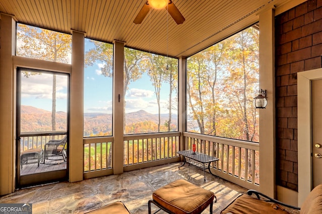 unfurnished sunroom with ceiling fan, a healthy amount of sunlight, a mountain view, and wooden ceiling