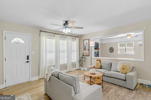 living room featuring a wall mounted air conditioner, light hardwood / wood-style flooring, and ceiling fan