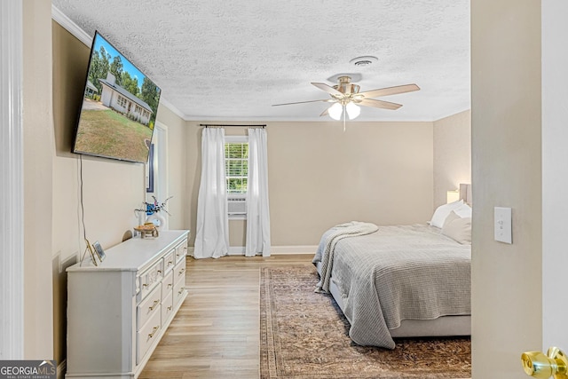 bedroom featuring ornamental molding, light wood-type flooring, a textured ceiling, and ceiling fan