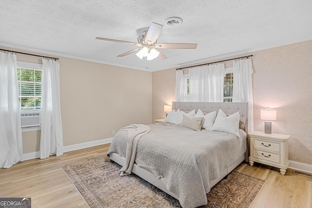 bedroom with cooling unit, a textured ceiling, light hardwood / wood-style flooring, and ceiling fan