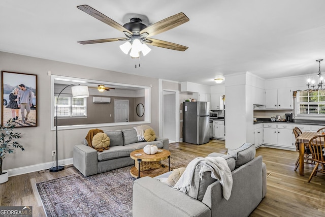 living room with ceiling fan with notable chandelier, light hardwood / wood-style floors, and an AC wall unit