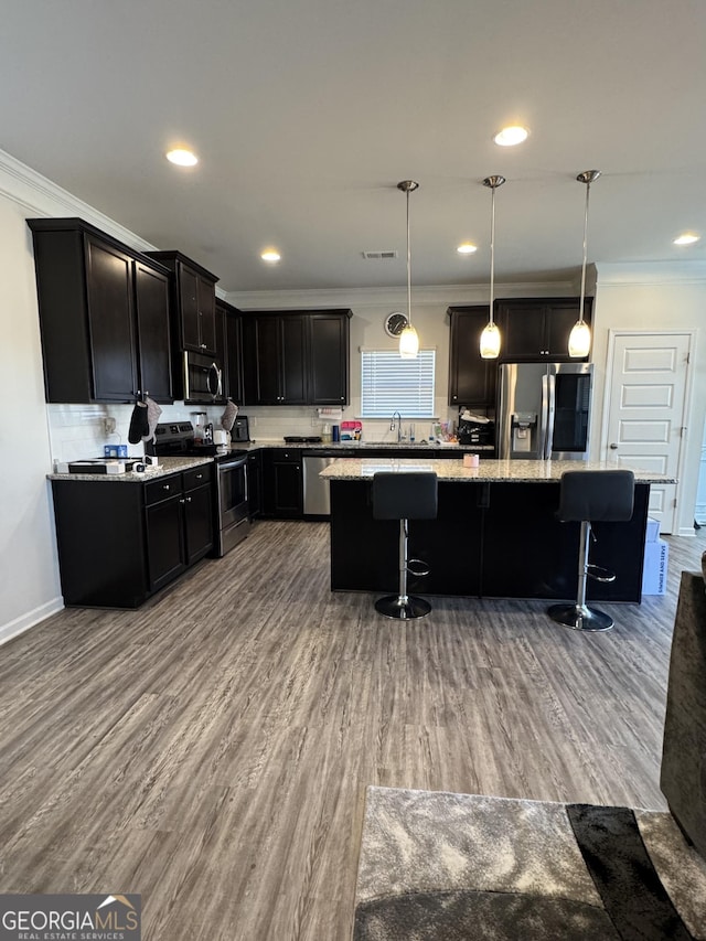 kitchen with appliances with stainless steel finishes, a kitchen island, a breakfast bar area, and pendant lighting