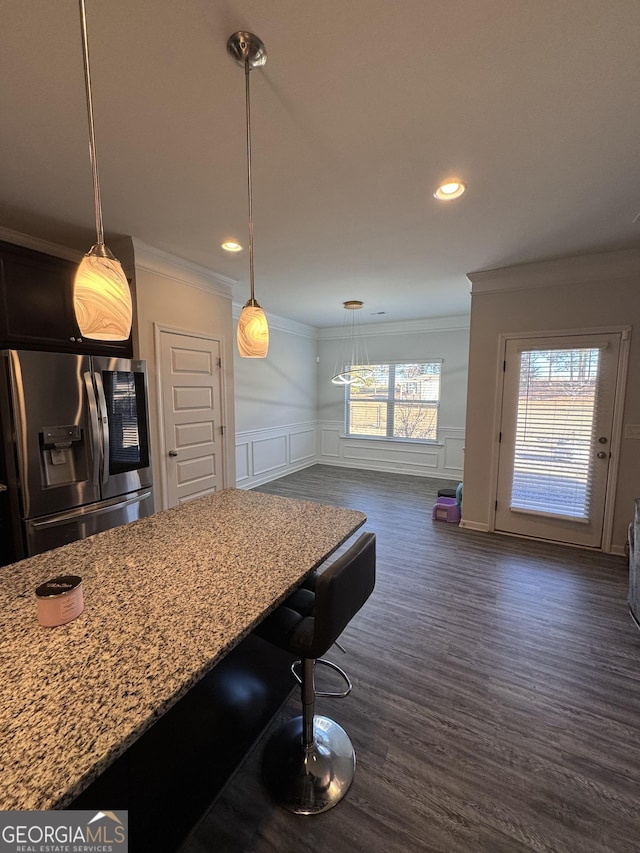 kitchen with stainless steel refrigerator with ice dispenser, dark hardwood / wood-style floors, light stone counters, and ornamental molding