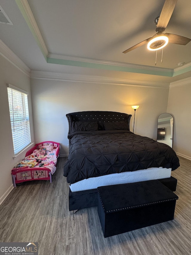 bedroom with ceiling fan, wood-type flooring, a tray ceiling, and crown molding