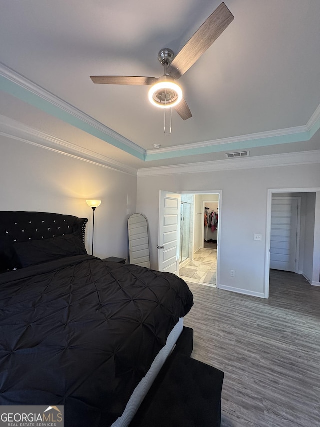 bedroom featuring ceiling fan, ornamental molding, a walk in closet, and a tray ceiling