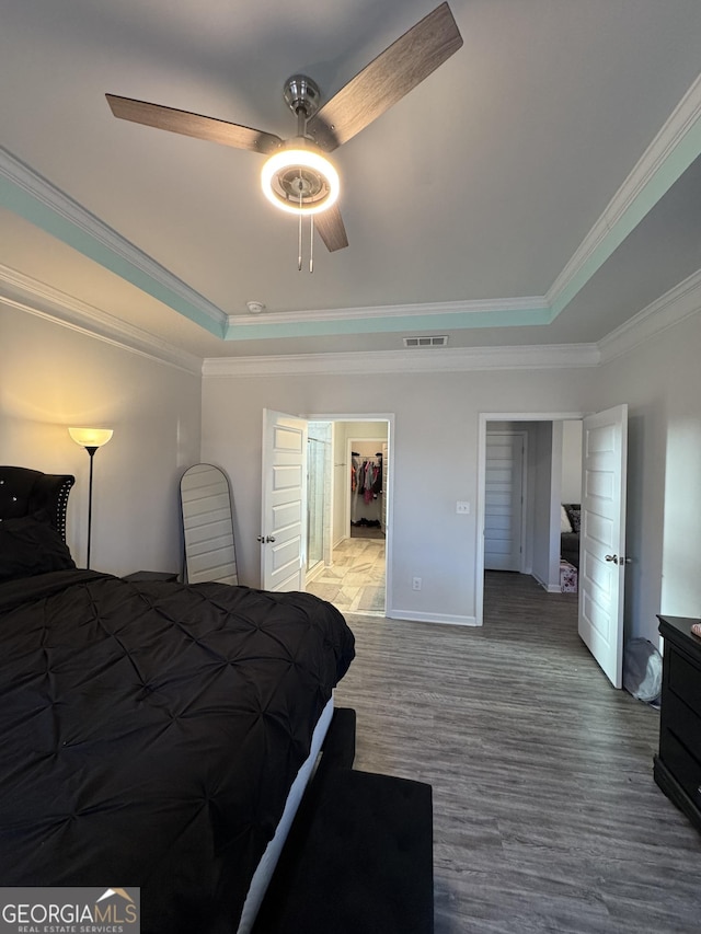 bedroom with ceiling fan, hardwood / wood-style floors, a raised ceiling, crown molding, and a spacious closet