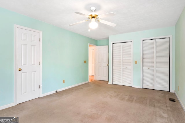 unfurnished bedroom featuring light colored carpet, two closets, and ceiling fan