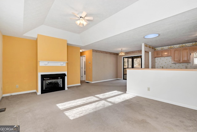 unfurnished living room featuring vaulted ceiling, light colored carpet, ceiling fan, and a tray ceiling