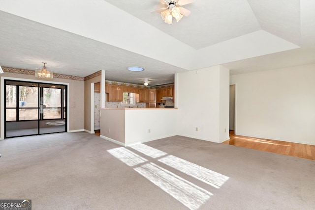 unfurnished living room featuring light colored carpet, a raised ceiling, and ceiling fan with notable chandelier