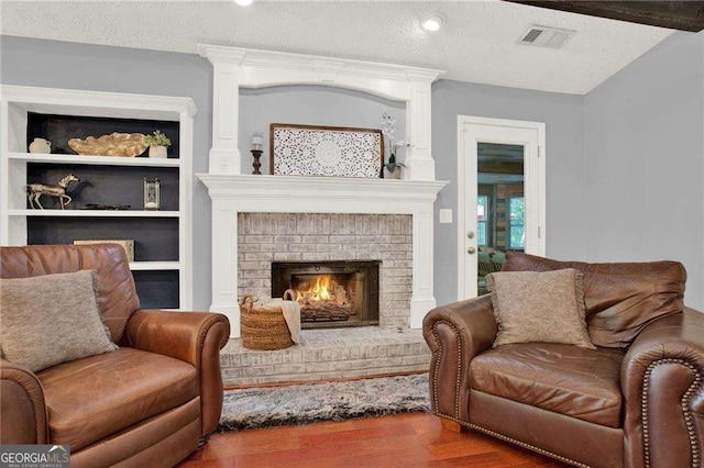 sitting room featuring a fireplace, a textured ceiling, built in shelves, and hardwood / wood-style flooring