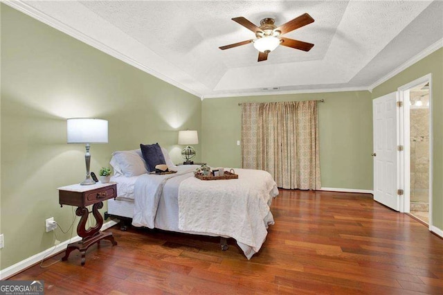 bedroom featuring ceiling fan, ornamental molding, dark hardwood / wood-style floors, a tray ceiling, and ensuite bathroom