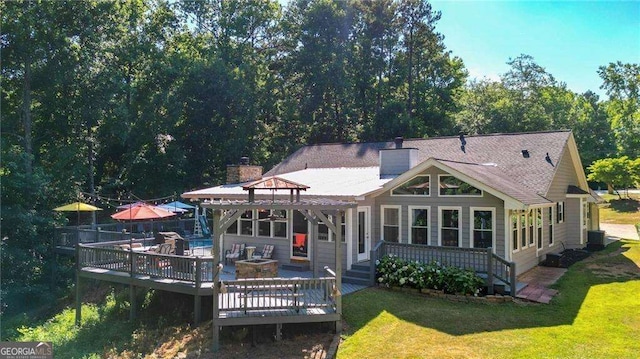 back of property with a gazebo, a pool side deck, a yard, and a fire pit