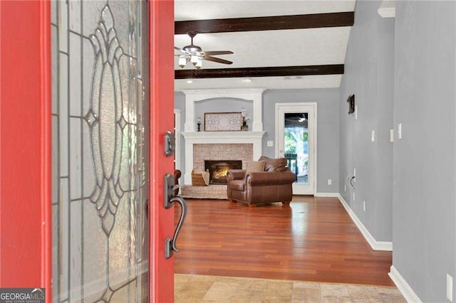 entrance foyer featuring a brick fireplace, ceiling fan, light wood-type flooring, and beamed ceiling