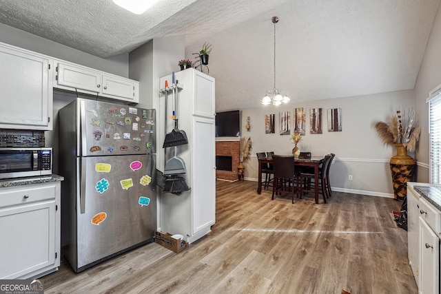 kitchen featuring a textured ceiling, a notable chandelier, white cabinets, appliances with stainless steel finishes, and a fireplace