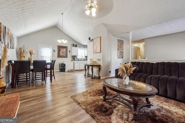 living room featuring ceiling fan with notable chandelier, a textured ceiling, vaulted ceiling, and light hardwood / wood-style floors