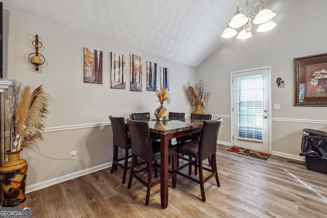 dining room with lofted ceiling, a textured ceiling, hardwood / wood-style floors, and an inviting chandelier