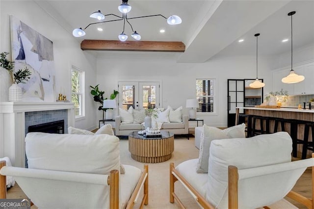 living room featuring a chandelier, a tile fireplace, french doors, ornamental molding, and beam ceiling