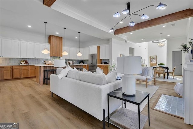 living room with ornamental molding, an inviting chandelier, beamed ceiling, and light wood-type flooring