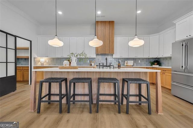 kitchen featuring white cabinets, high end fridge, a kitchen island with sink, and hanging light fixtures