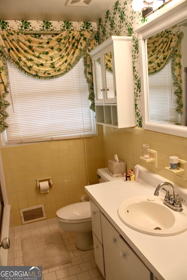 bathroom with toilet, vanity, tile patterned floors, and tile walls