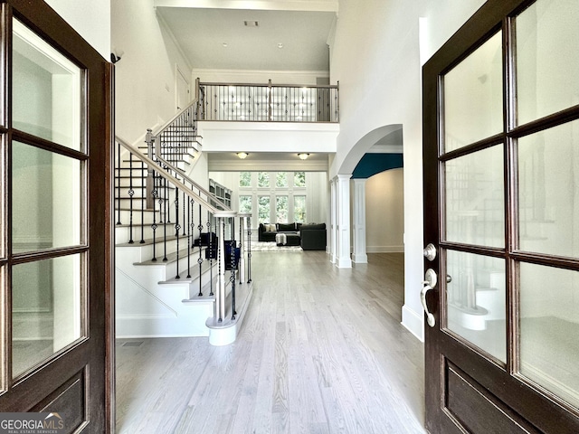 foyer featuring a high ceiling, decorative columns, ornamental molding, and wood-type flooring